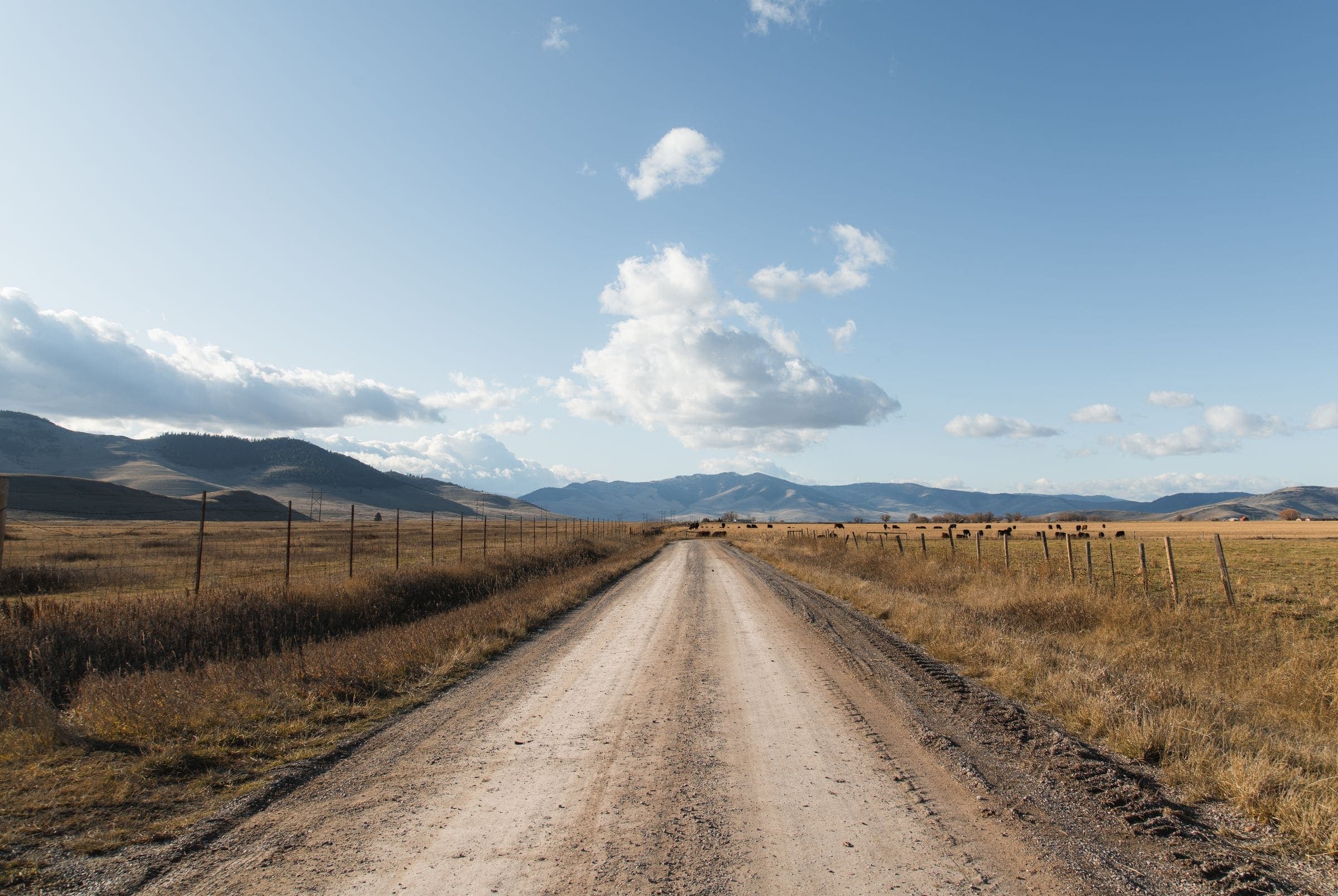A gravel road with fence lines running toward distant hills, near our windshield replacement New Underwood SD service area